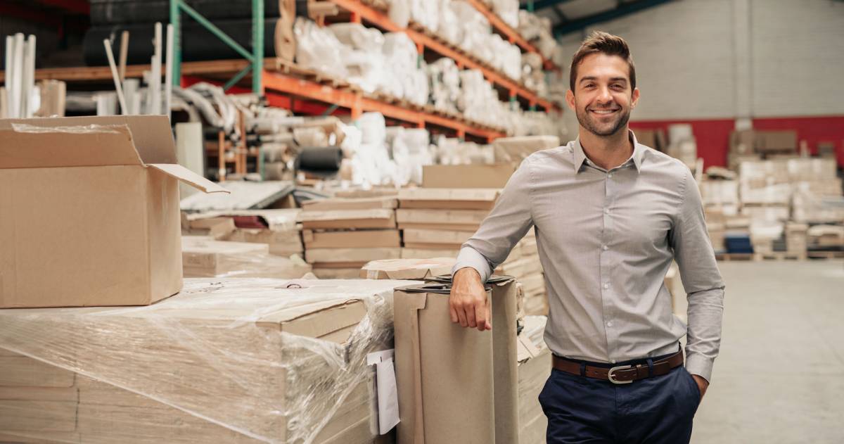 Manager glimlachend terwijl hij tegen de voorraad leunt in een groot magazijn