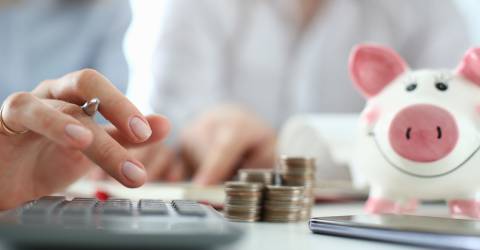 man en vrouw aan tafel met rekenmachine, geld en spaarvarken